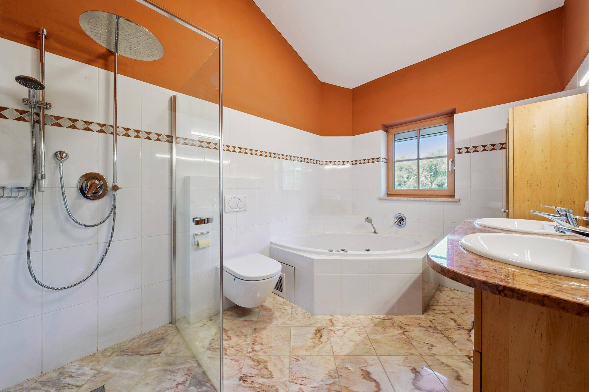 Badezimmer mit großer Dusche, Eckbadewanne, Doppelwaschbecken und Fenster.