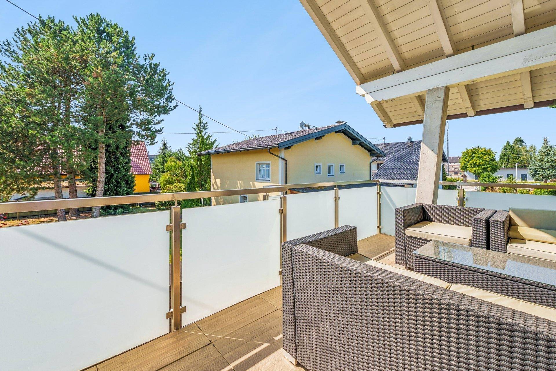 Möblierter Balkon mit Rattan-Sitzgruppe und Blick auf die umliegende Wohngegend und Bäume.