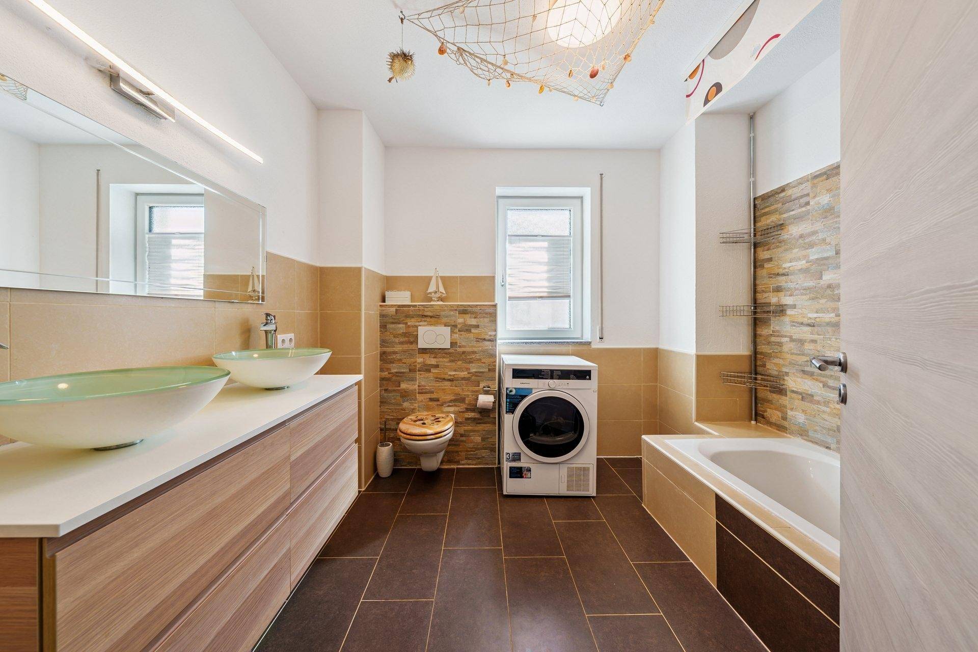 Modernes Badezimmer mit Doppelwaschbecken, Badewanne, WC und Waschmaschine.