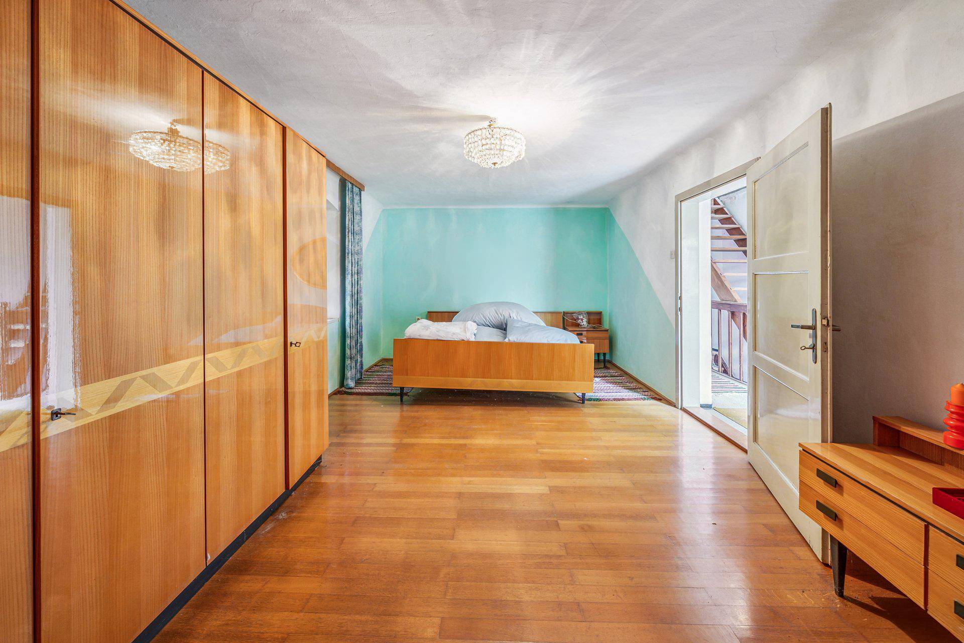 Helles Schlafzimmer mit Holzboden, integriertem Kleiderschrank und Zugang zu einem Balkon.