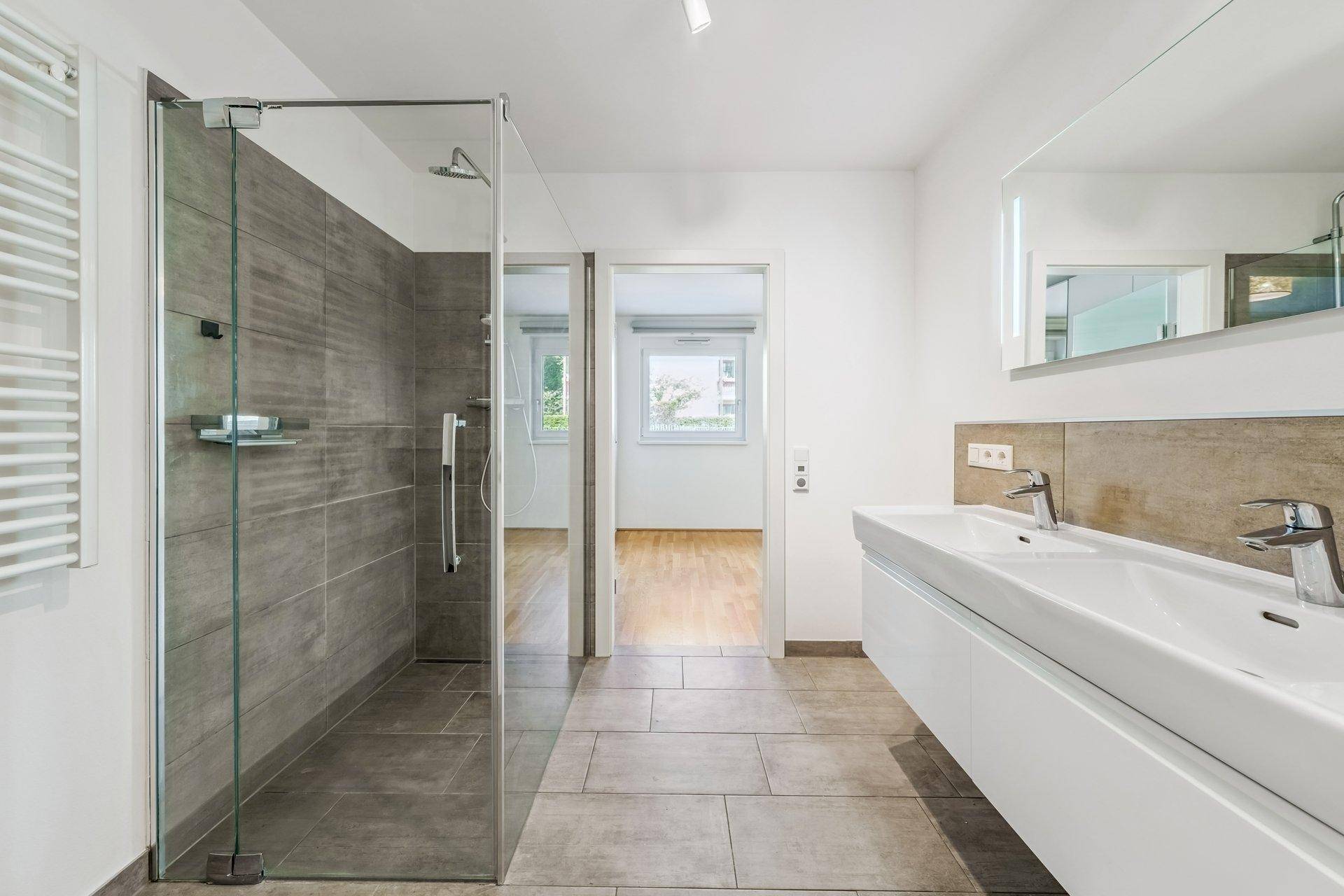 Modernes Badezimmer mit begehbarer Dusche, Doppelwaschbecken und großen Fliesen.
