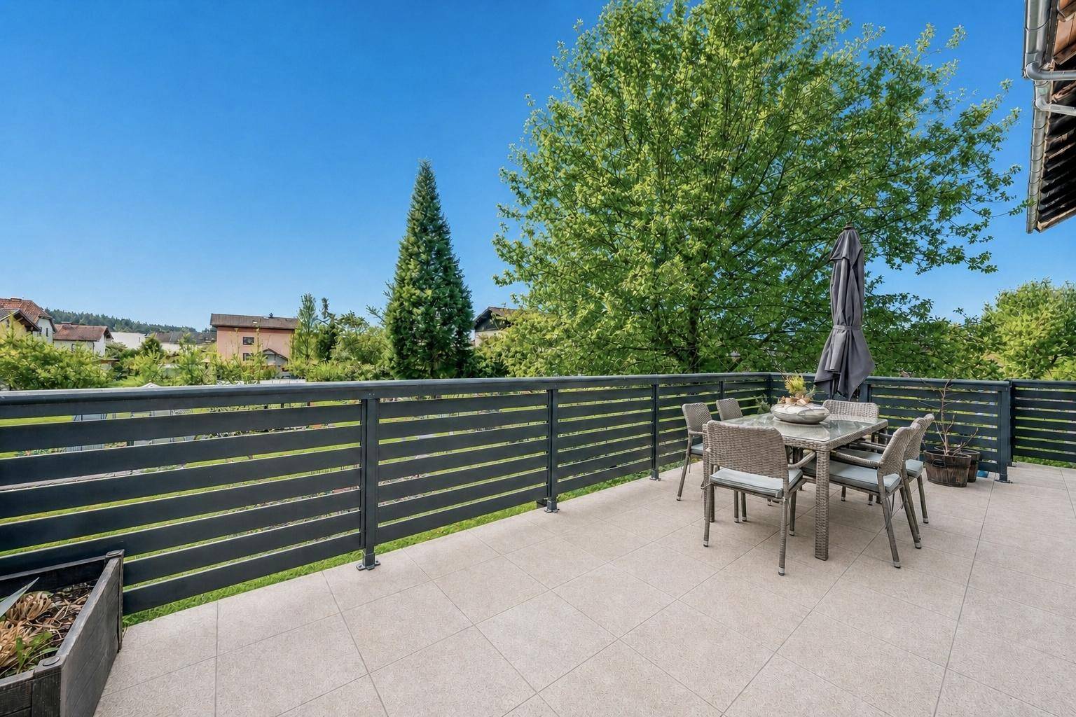 Geräumige Terrasse mit modernen Fliesen, Esstisch und Blick ins Grüne unter blauem Himmel.