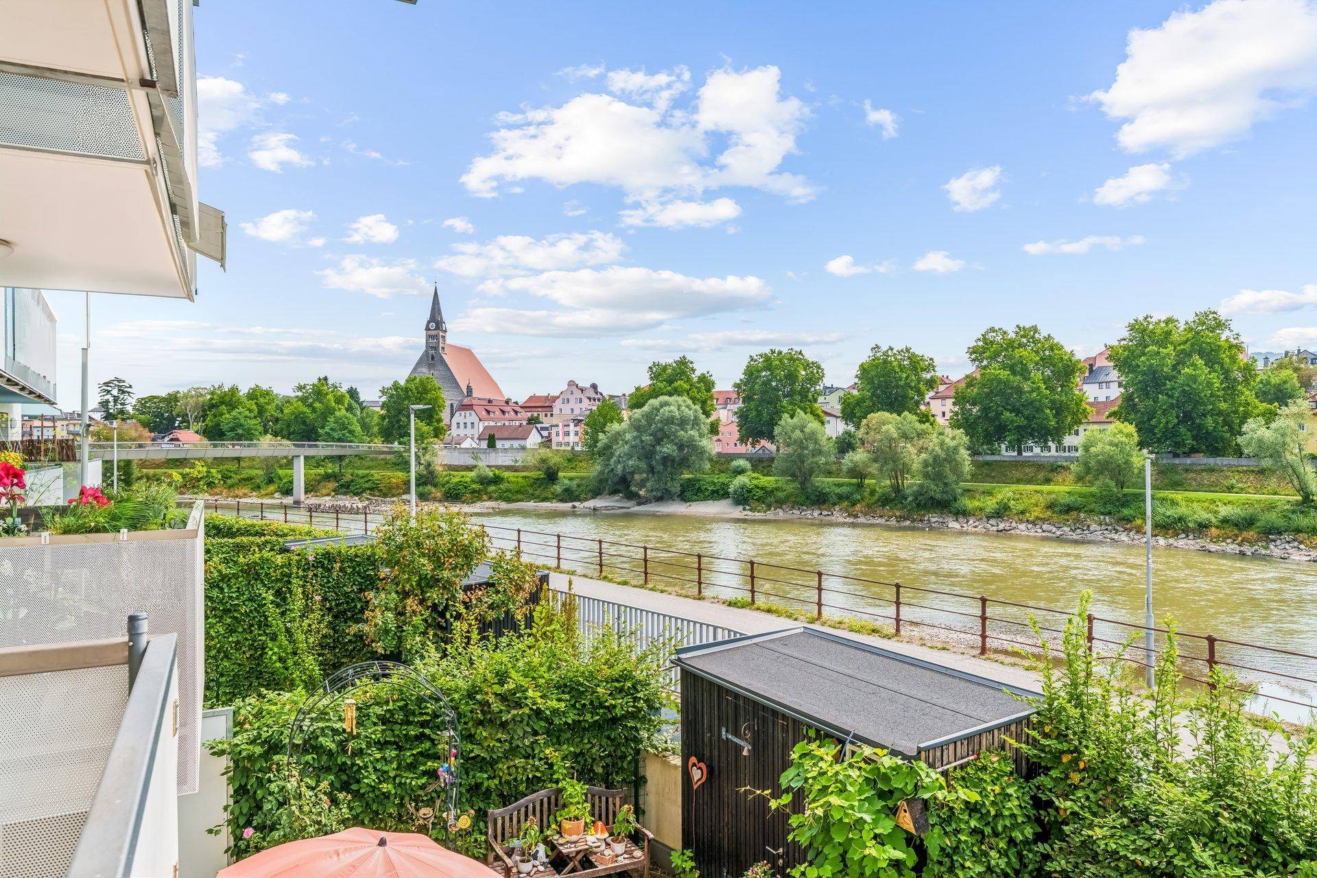 Blick vom Balkon auf den Fluss, eine historische Kirche und die grüne Umgebung.