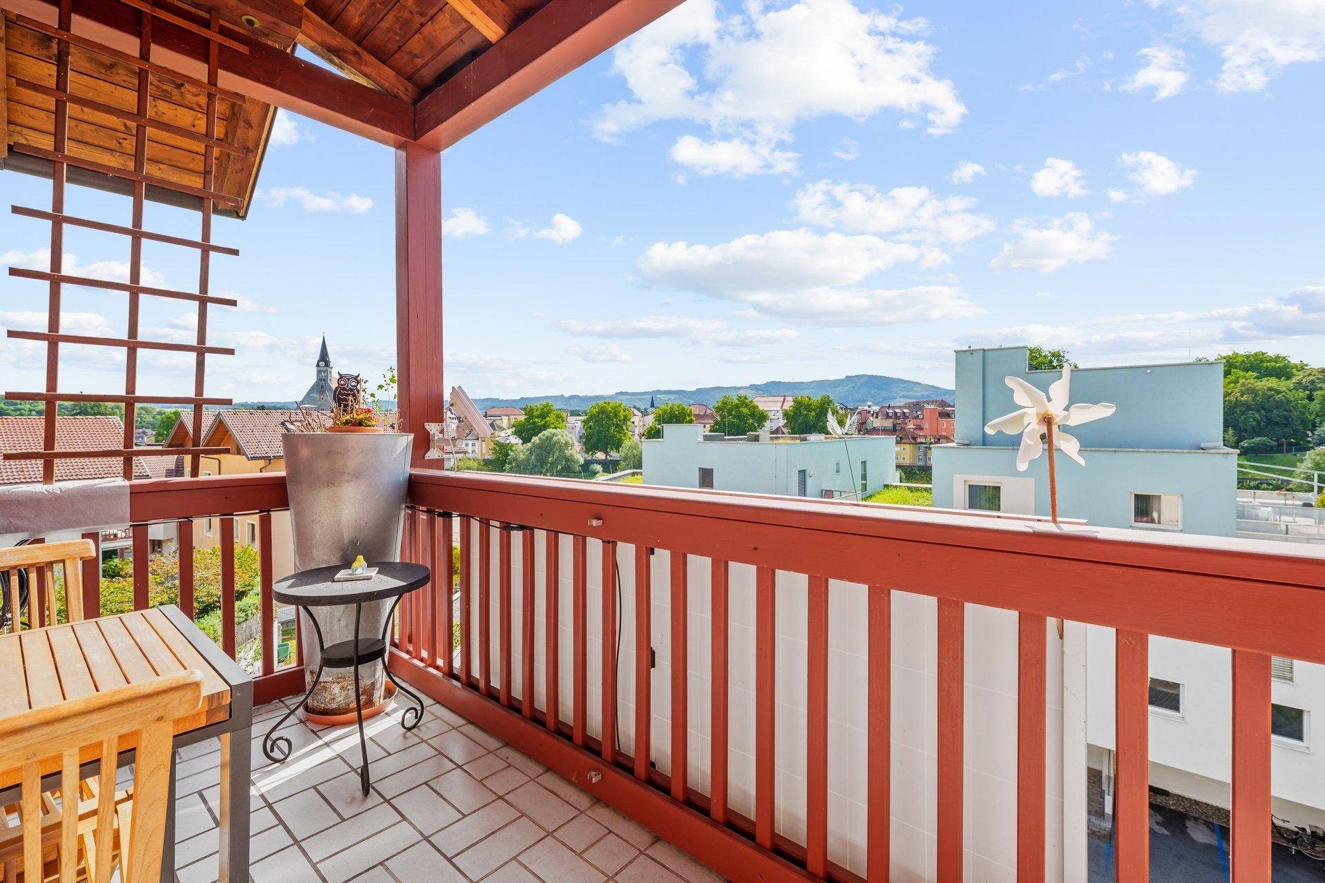 Sonniger Balkon mit Sitzgelegenheiten und weitem Blick über die Stadt und die grüne Landschaft.