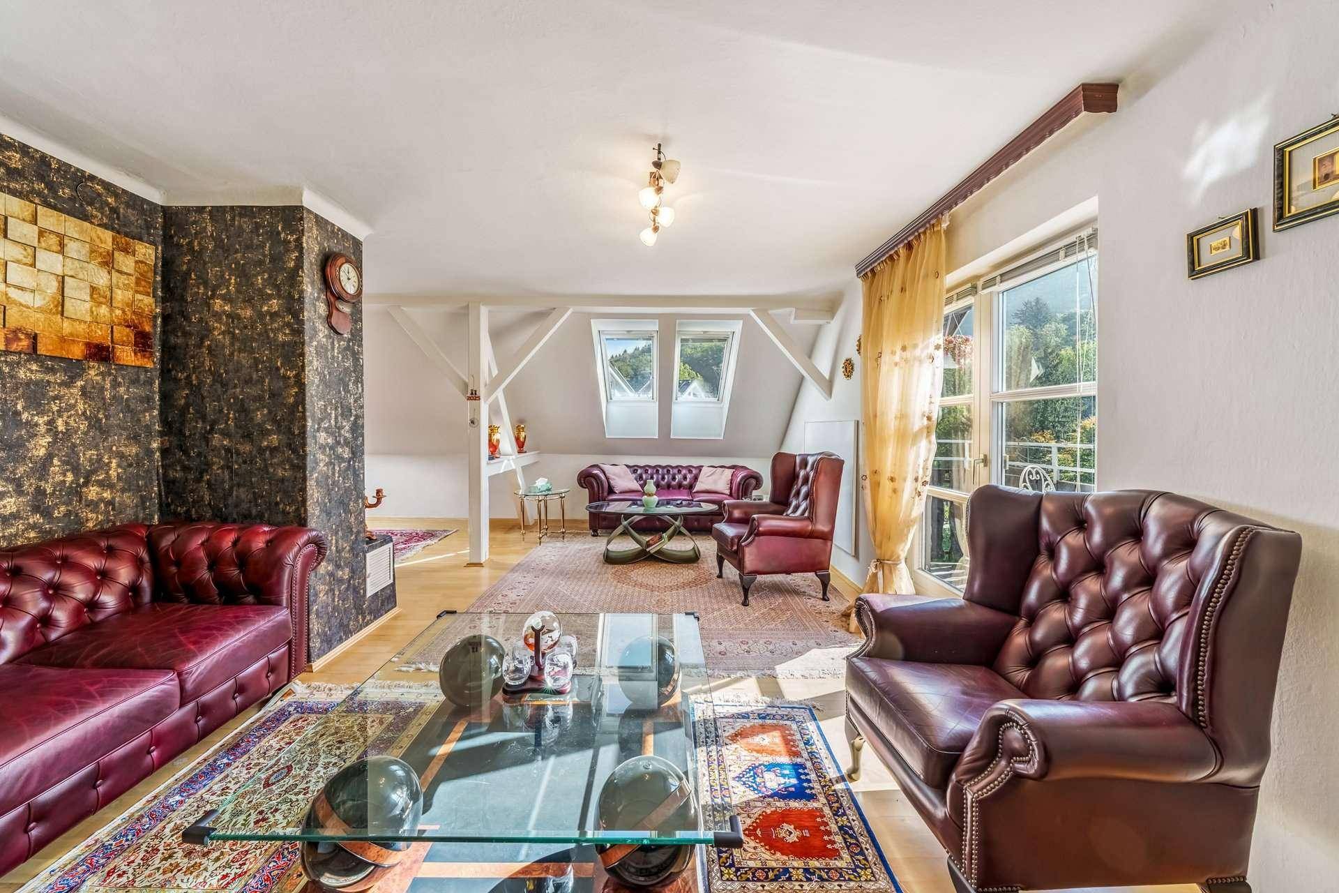 Geräumiges Wohnzimmer mit Ledersofas, Holzbalken und Dachschrägenfenstern.