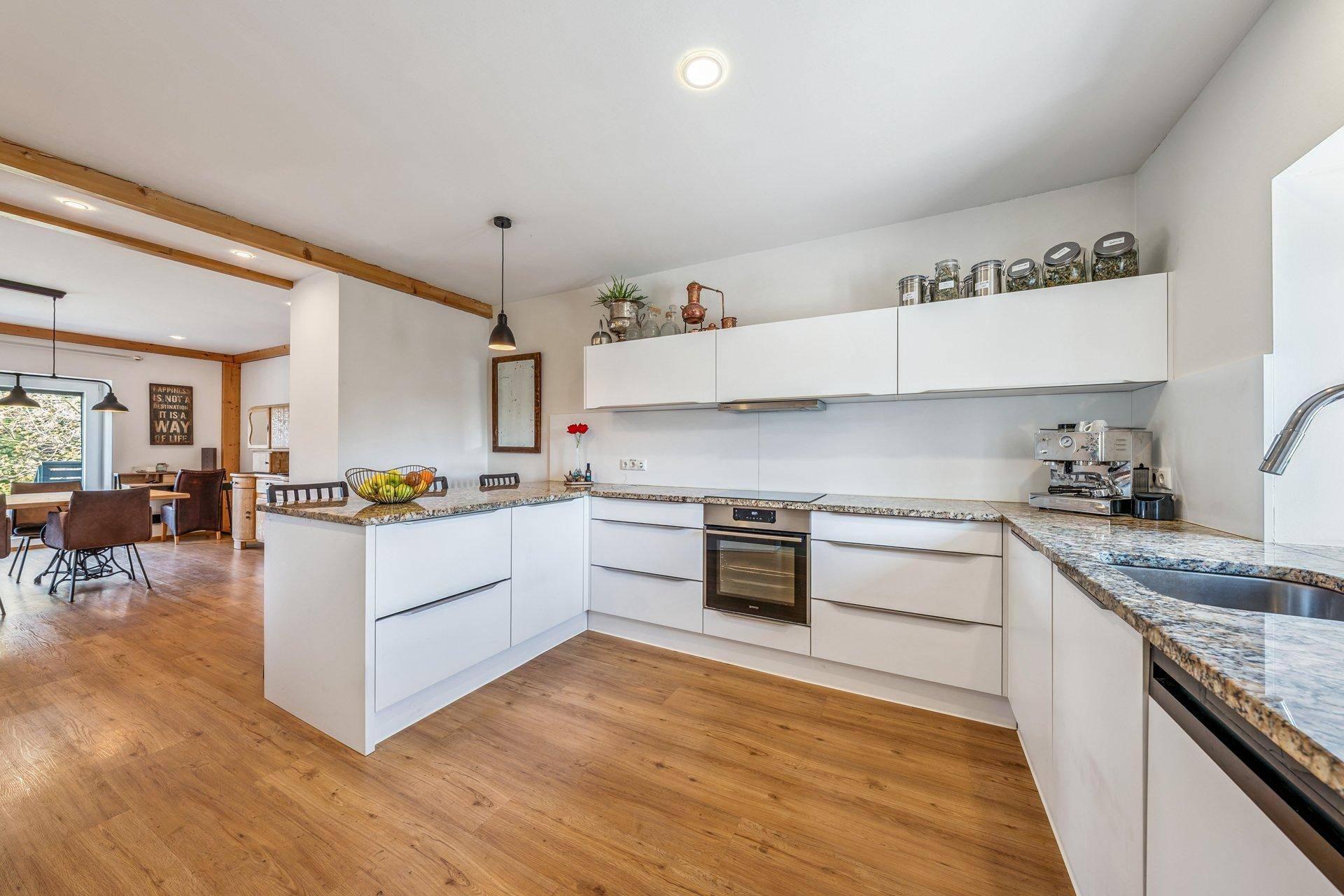 Moderne weiße Küche mit Kücheninsel, Granitarbeitsplatten und integrierten Geräten.