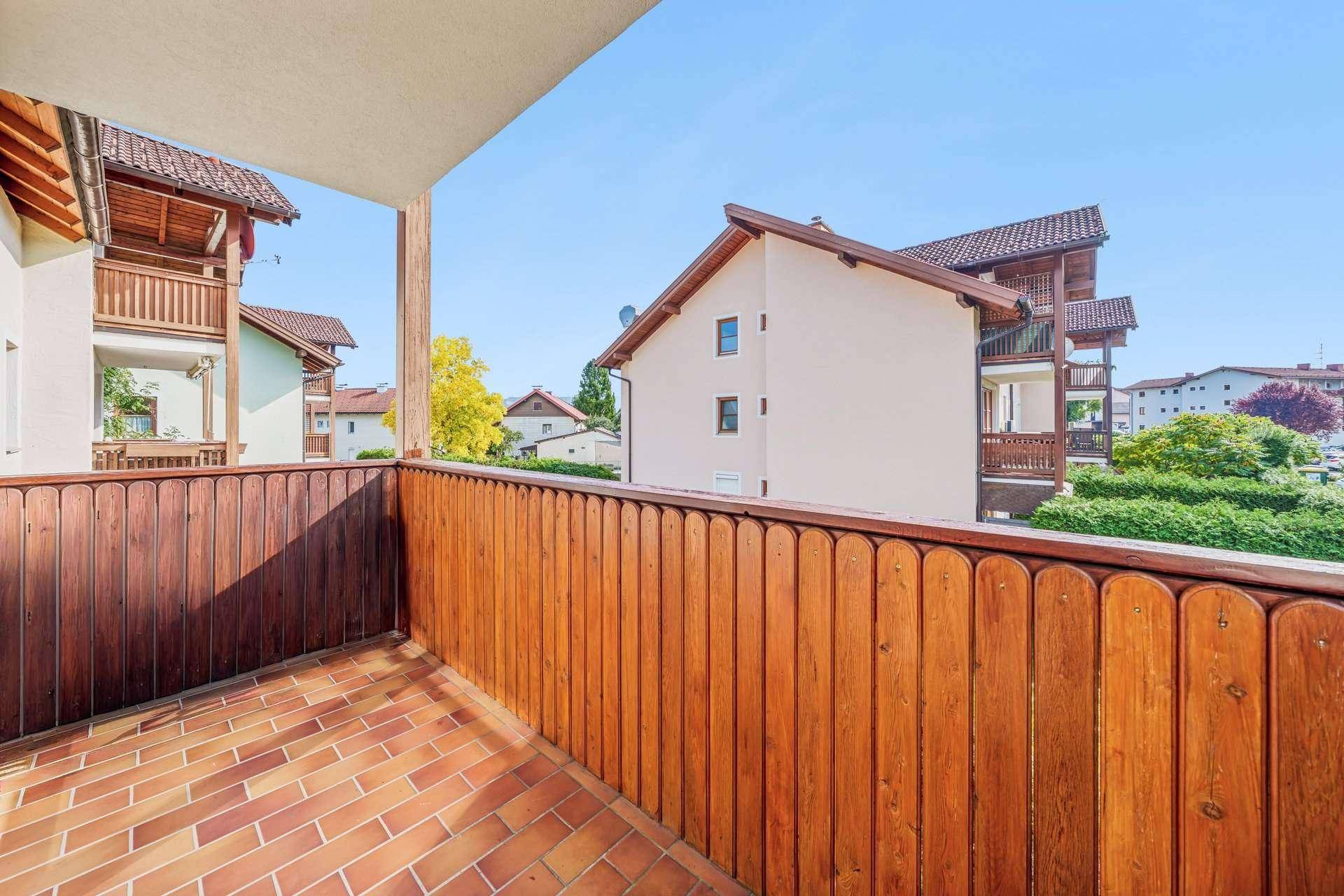 Balkon mit Holzbalkonbrüstung und Fliesenboden, bietet Blick auf umliegende Gebäude.