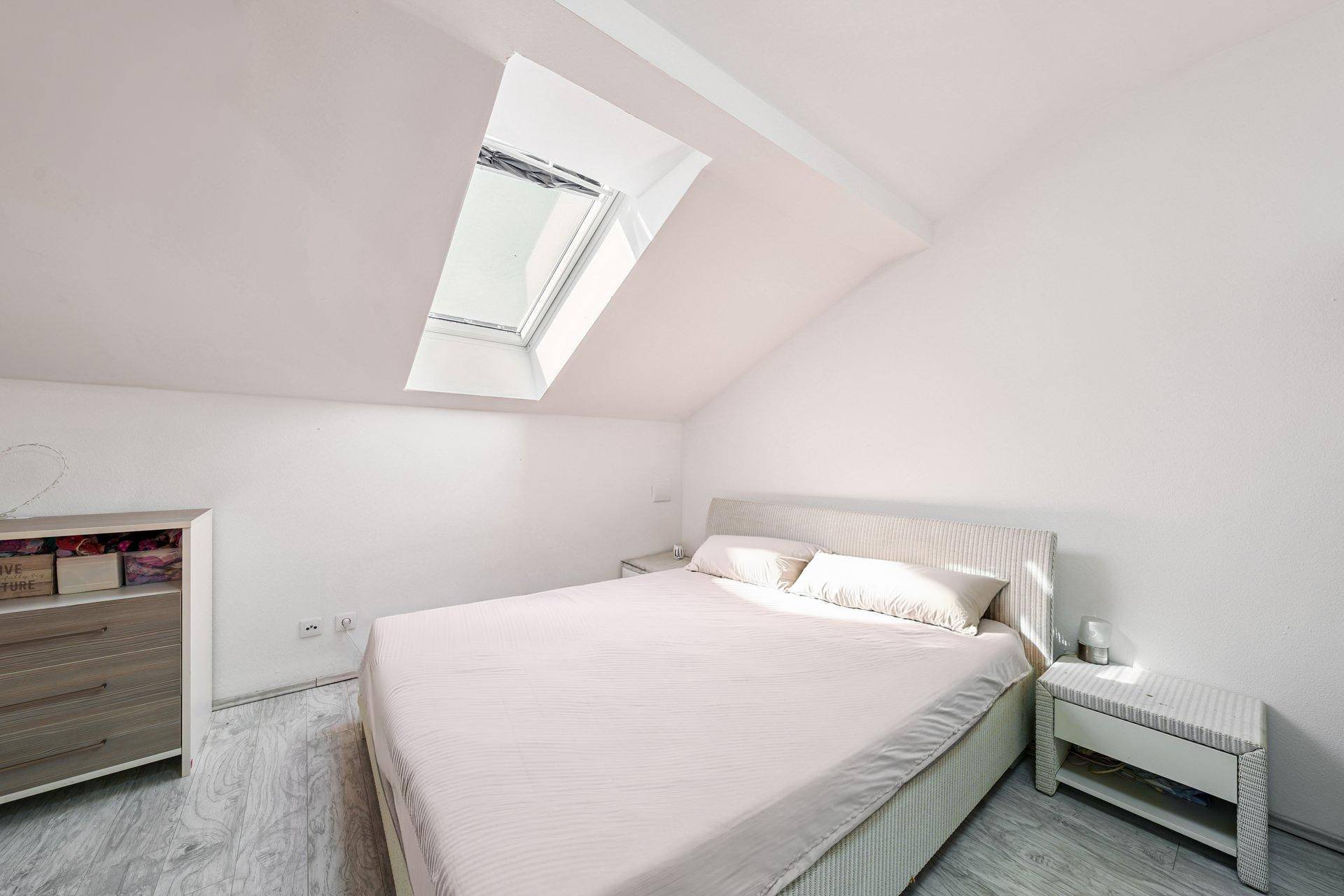 Helles Schlafzimmer im Dachgeschoss mit Dachfenster und modernem Laminatboden.