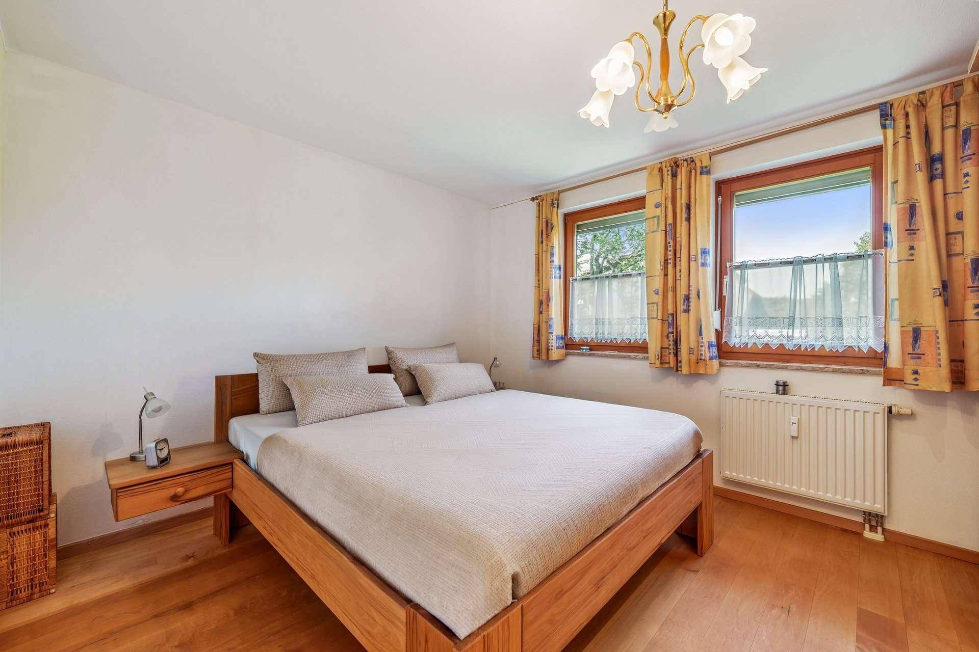 Gemütliches Schlafzimmer mit Holzdoppelbett, zwei Fenstern und hellem Holzfußboden.