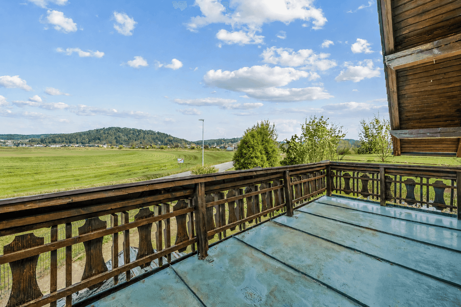 Holzbalkon mit traditionellem Geländer und weitem Blick über grüne Felder und die umliegende Landschaft.