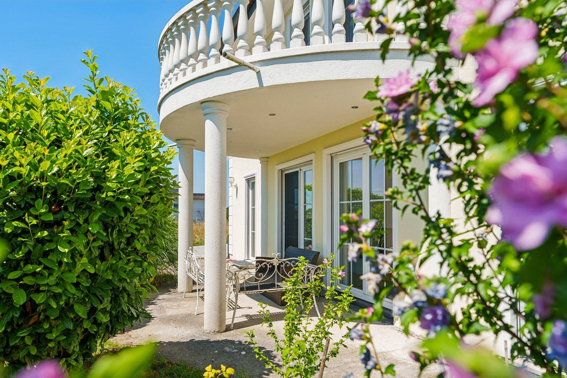 Überdachte Terrasse mit Sitzgelegenheiten und blühenden Pflanzen im Gartenbereich.