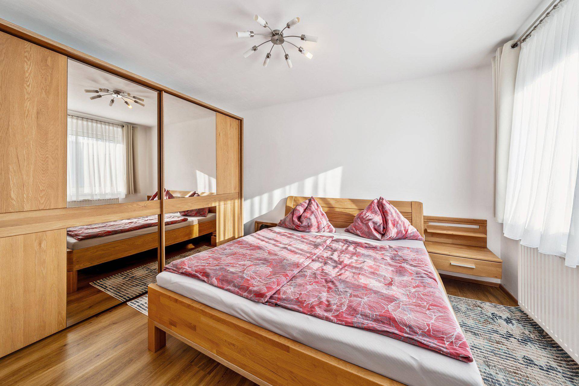Helles Schlafzimmer mit Holzbett, passenden Nachttischen und großem Spiegelschrank.