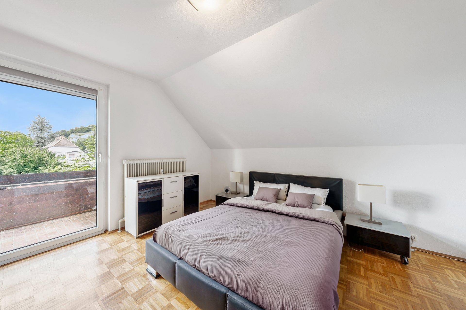 Helles Schlafzimmer mit Doppelbett, Dachschrägen und Zugang zu einem Balkon.