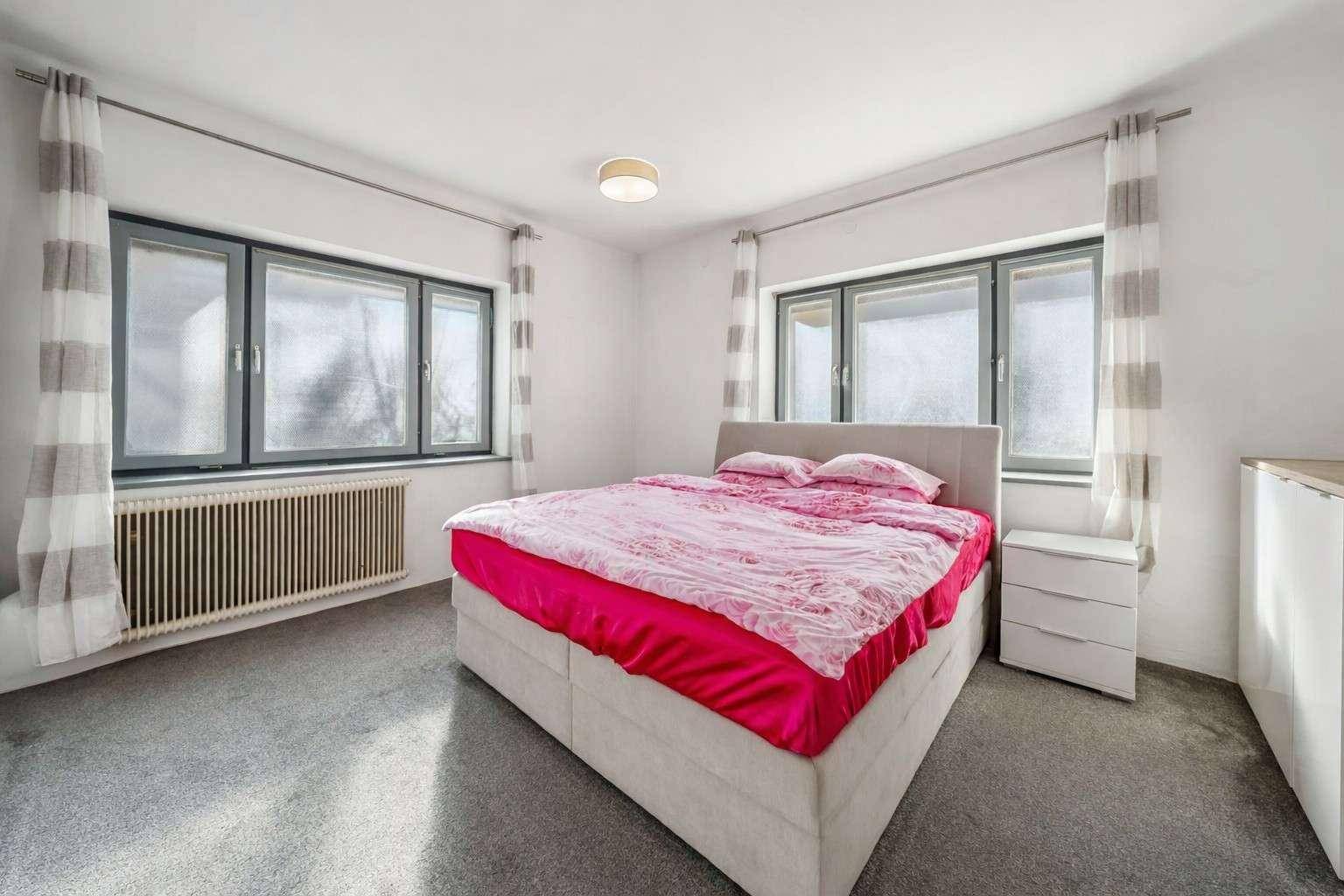 Helles Schlafzimmer mit Doppelbett, Teppichboden und zwei großen Fenstern.