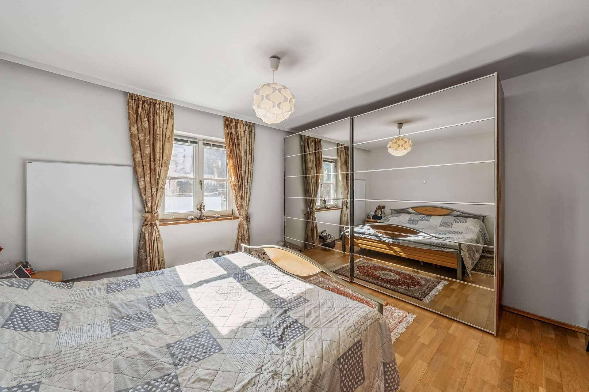 Helles Schlafzimmer mit Holzboden, Spiegelschrank und natürlichem Lichteinfall.