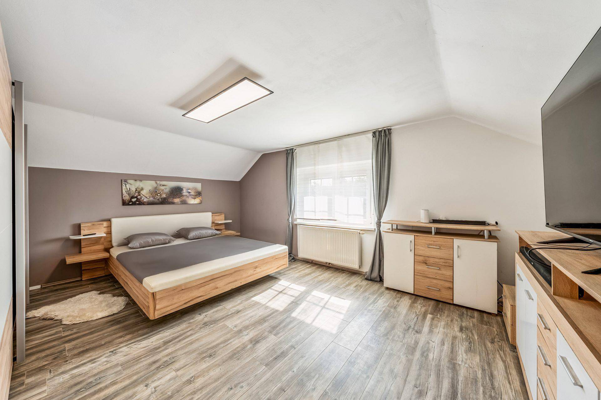 Helles Schlafzimmer mit modernem Holzbett, Laminatboden und Dachschräge.