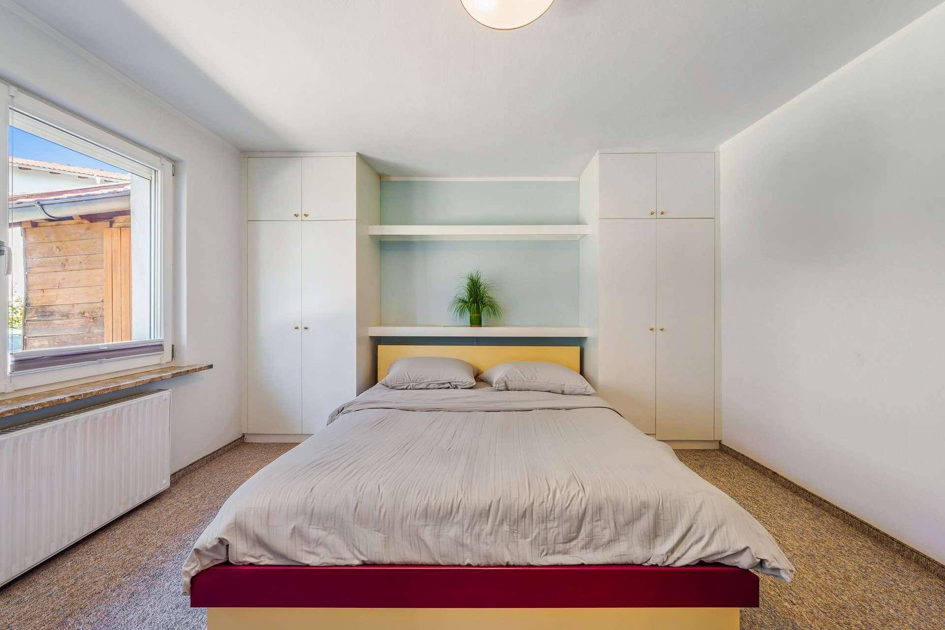 Helles Schlafzimmer mit integrierten Einbauschränken, Doppelbett und Fenster für Tageslicht.