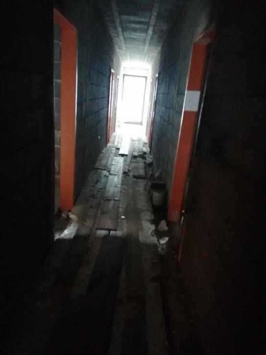 Langer, dunkler Flur in einem Rohbau mit Holzdielen auf dem Boden und sichtbaren Türrahmen.