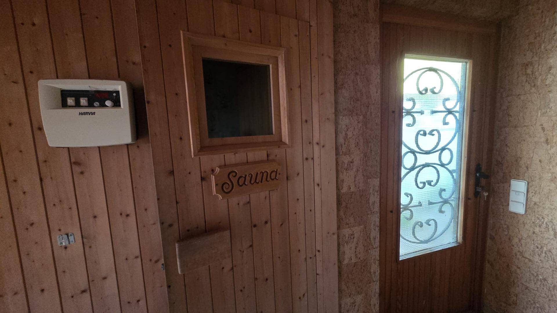 Holzvertäfelte Sauna mit Bedienfeld und einer Tür mit dekorativem Glaseinsatz.