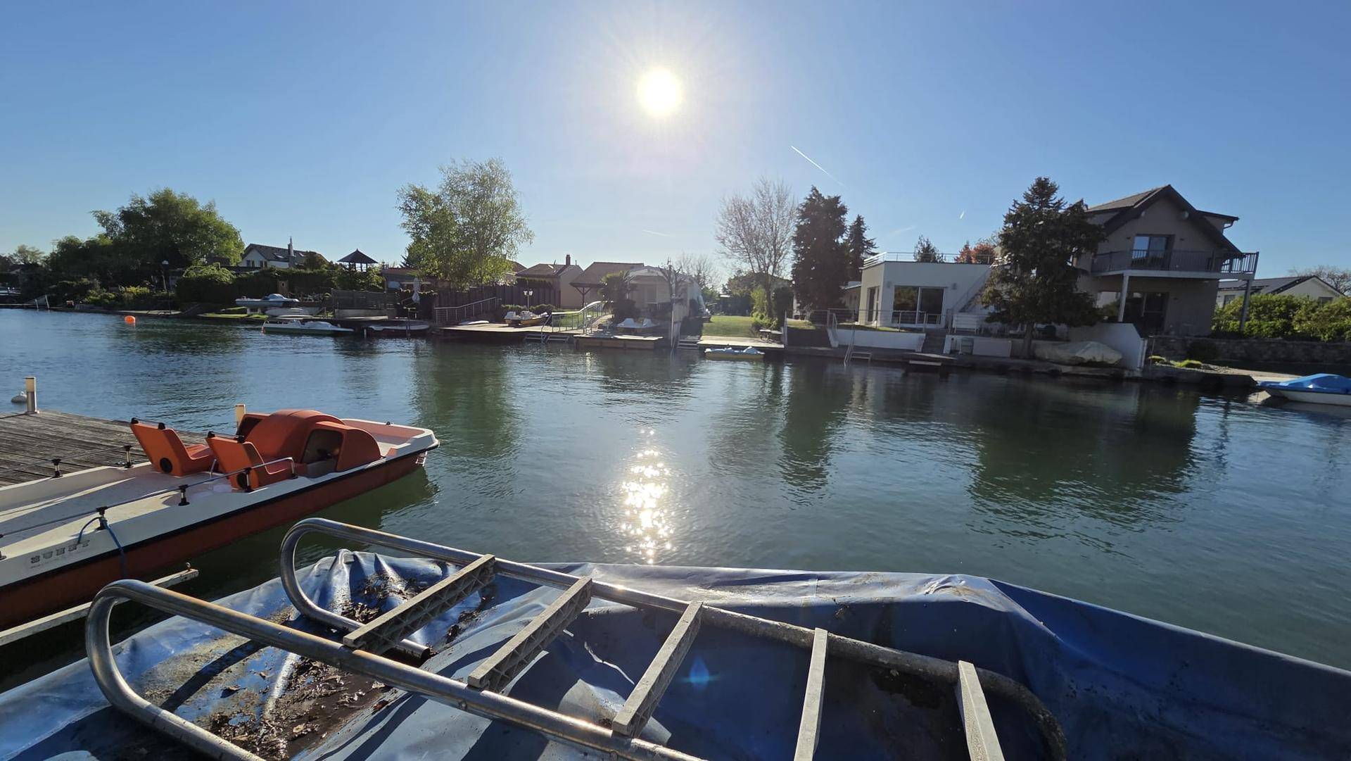 Nahaufnahme eines Bootes mit Leiter, Blick über den sonnigen Kanal zu den gegenüberliegenden Häusern.