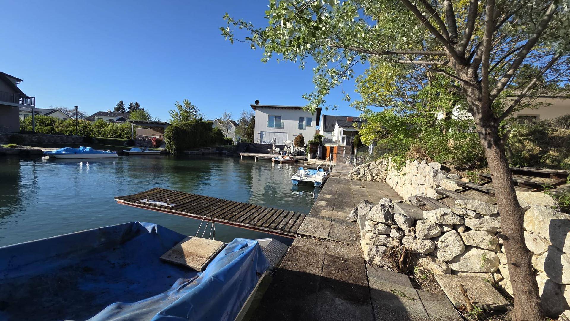Panoramablick auf den Kanal mit einem Holzsteg, einem Boot und der umliegenden Wohnbebauung.