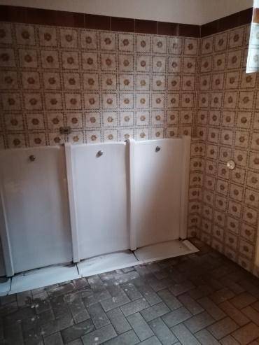 Badezimmer mit gemusterten Fliesen an den Wänden, dunklem Fliesenboden und drei Urinalen.