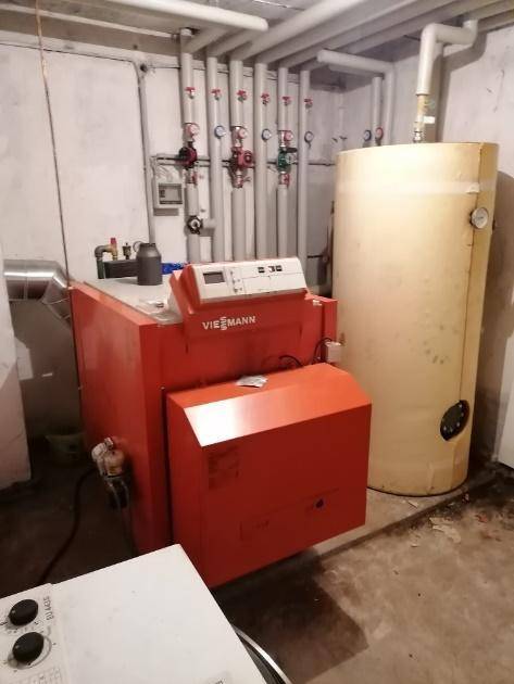 Heizungsraum mit großem Warmwasserspeicher und Viessmann-Heizkessel, umgeben von Rohren.