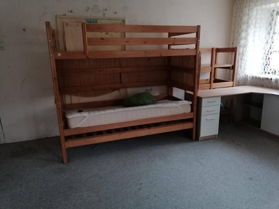 Schlafzimmer mit einem hölzernen Etagenbett, einem Schreibtisch und grauem Teppichboden.