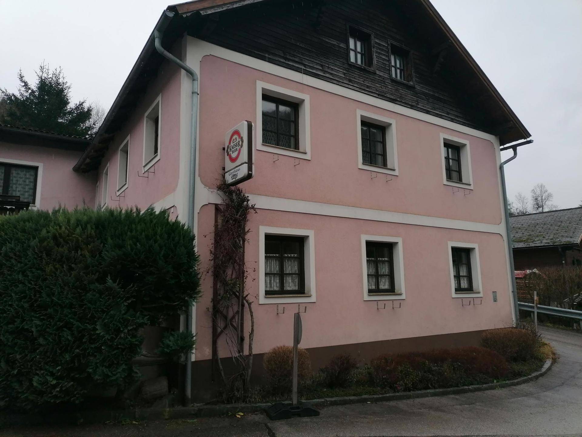 Rosa gestrichenes Gebäude mit traditioneller Architektur, Holzbalkonen und einem Werbeschild an der Fassade.