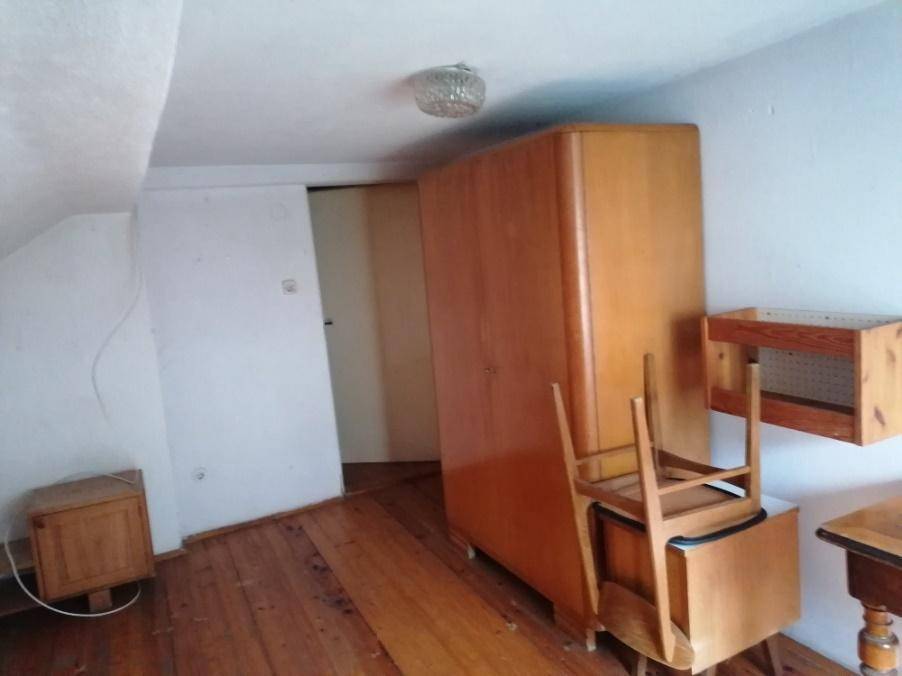 Dachzimmer mit schräger Decke, Holzdielenboden und einem Holzschrank, der den Raum gemütlich macht.