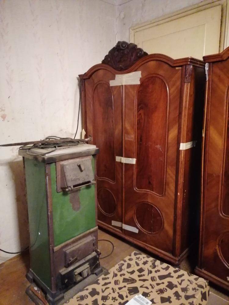 Raum mit einem alten grünen Holzofen und großen, verzierten Holzschränken, die einen traditionellen Charme verleihen.