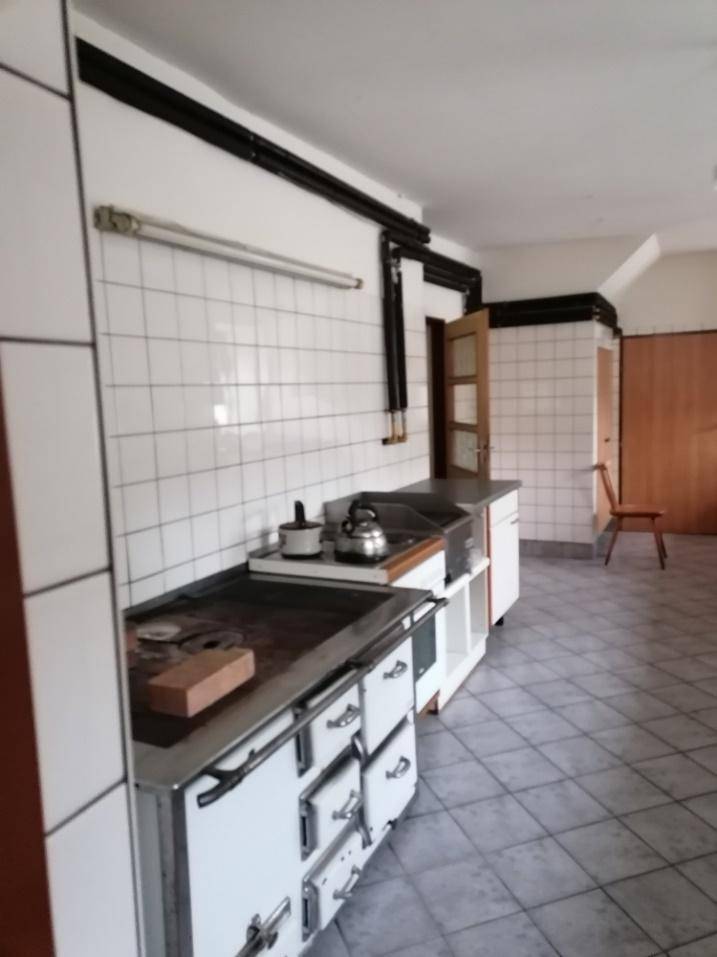 Geräumige Küche mit weißen Fliesenwänden, traditionellem Herd und Arbeitsflächen, bereit zum Kochen.
