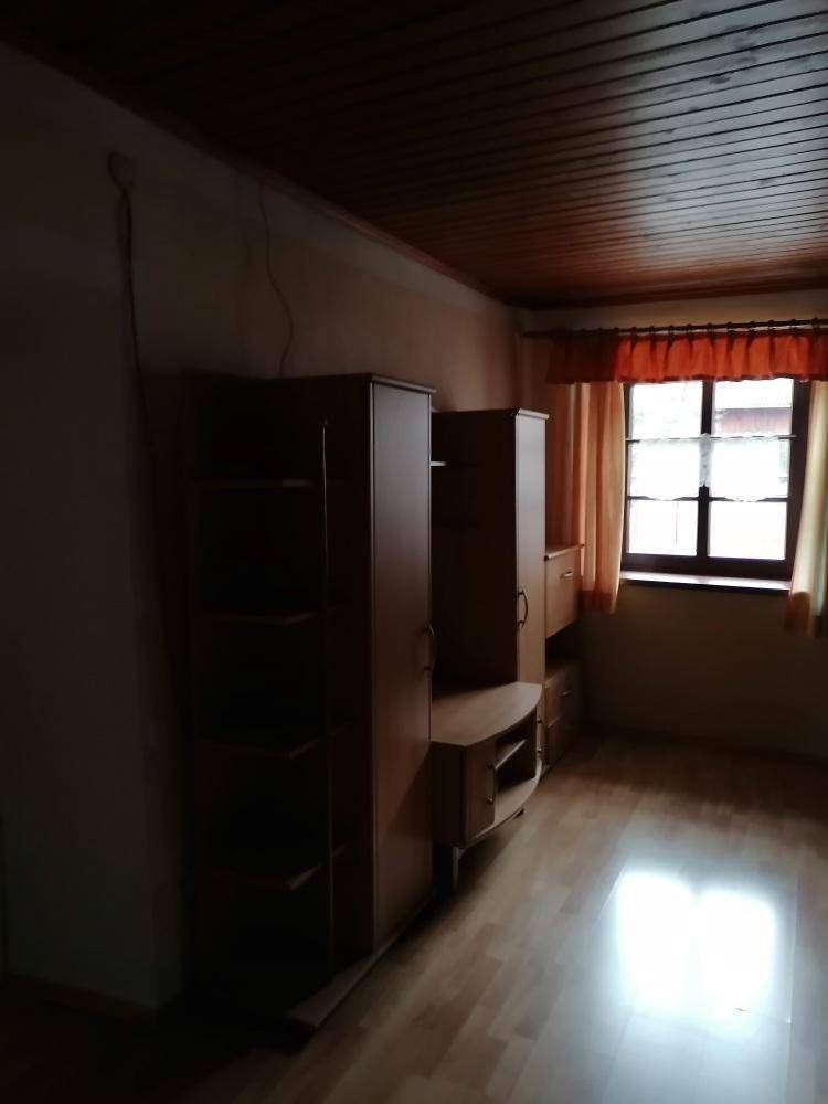 Schlafzimmer mit Holzdecke, Laminatboden und einem Fenster mit Vorhängen, das auf eine Renovierung wartet.