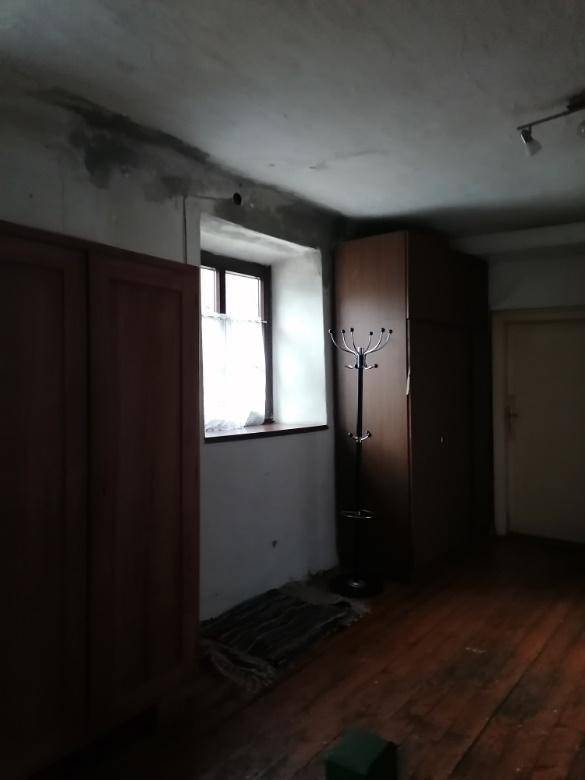 Dunkler Flur mit Holzdielenboden, einem kleinen Fenster und alten Kleiderschränken, die Renovierung benötigen.