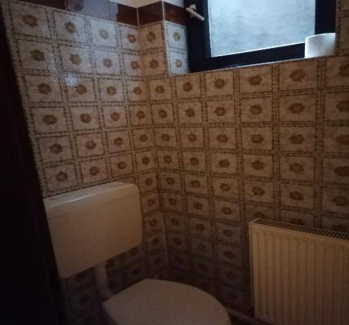 Kleines WC mit gemusterten Fliesen, Toilette und Heizkörper, beleuchtet durch ein kleines Fenster.