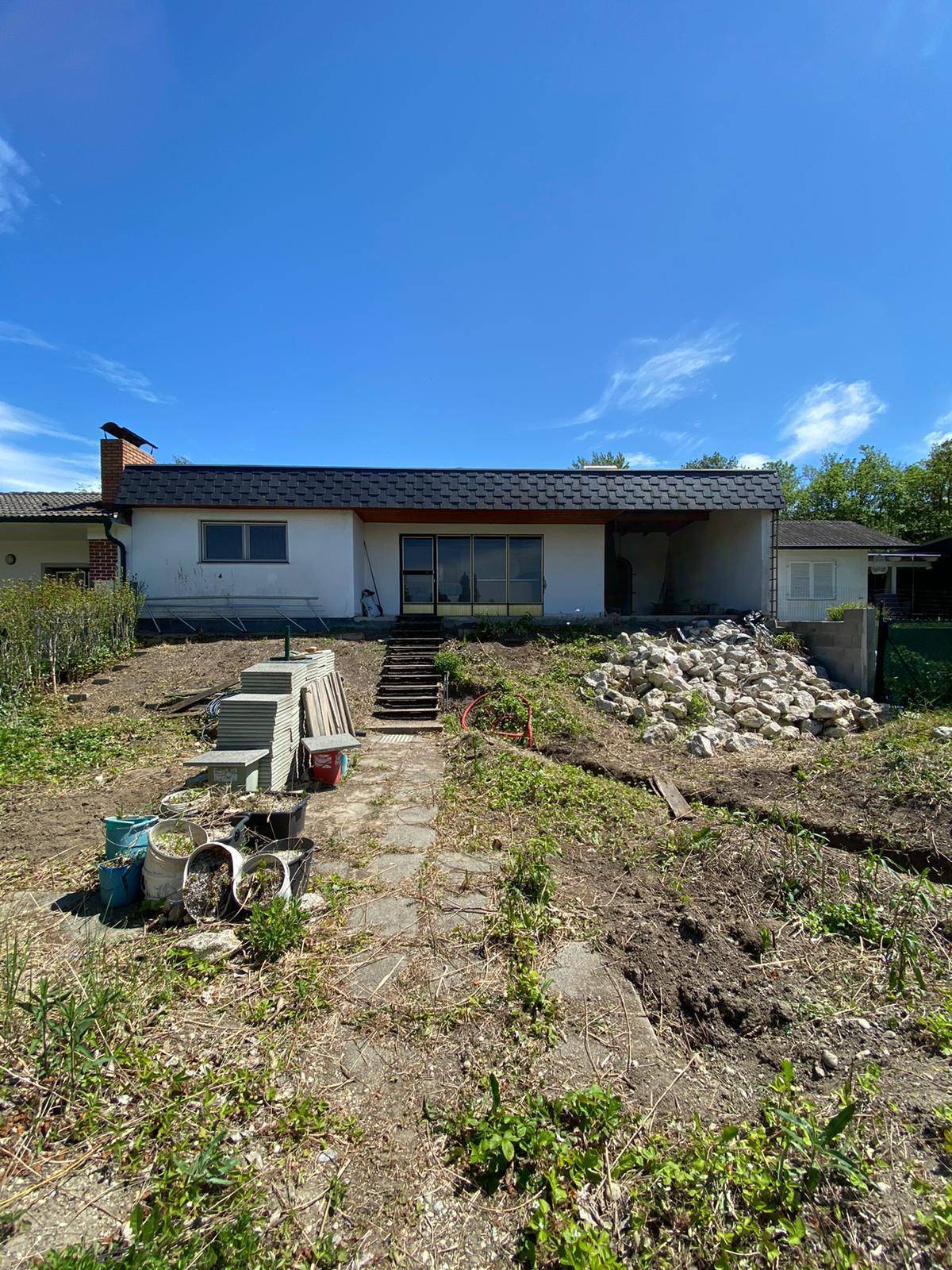 Rückseite eines Hauses mit großem, ungepflegtem Garten und sichtbaren Baumaterialien.