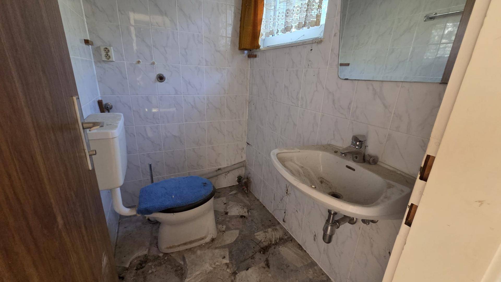 Kleines Badezimmer oder Gäste-WC im Renovierungszustand mit alten Fliesen, Toilette und Waschbecken.