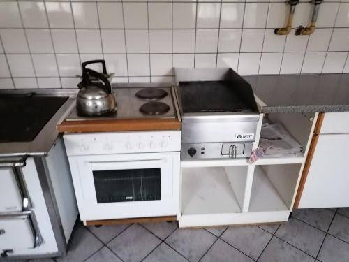 Gewerbliche Küche mit Herd, Backofen und Grillplatte, umgeben von weißen Fliesen und Arbeitsflächen.