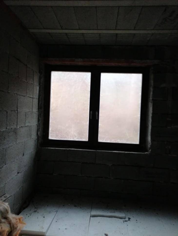 Dunkler Raum im Rohbau mit unverputzten Ziegelwänden und einem Fenster, der auf Fertigstellung wartet.