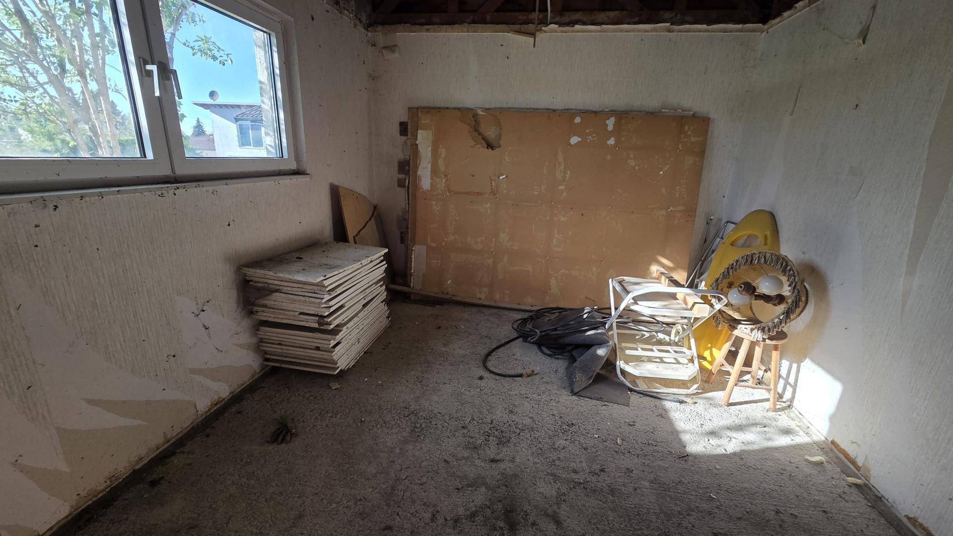 Renovierungsbedürftiger Raum mit Fenster, Betonboden und gestapelten Baumaterialien.