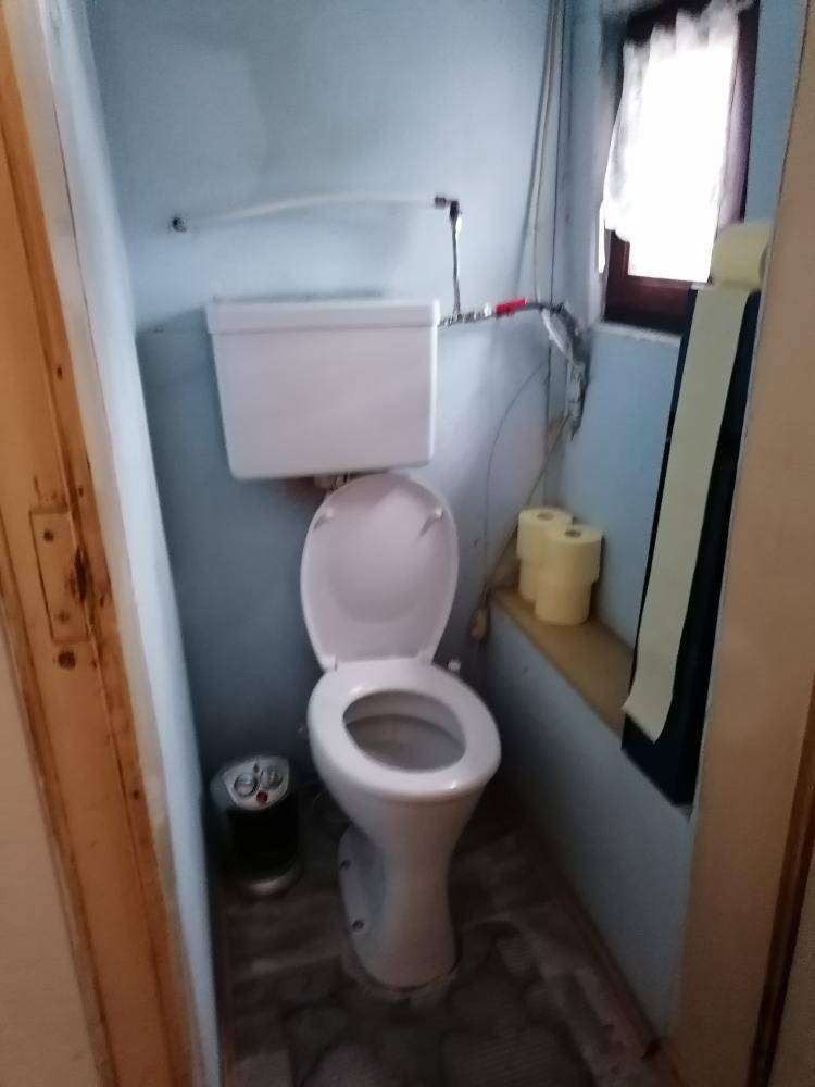 Kleine Toilette mit WC, blauen Wänden und einem kleinen Fenster, das für Belüftung sorgt.