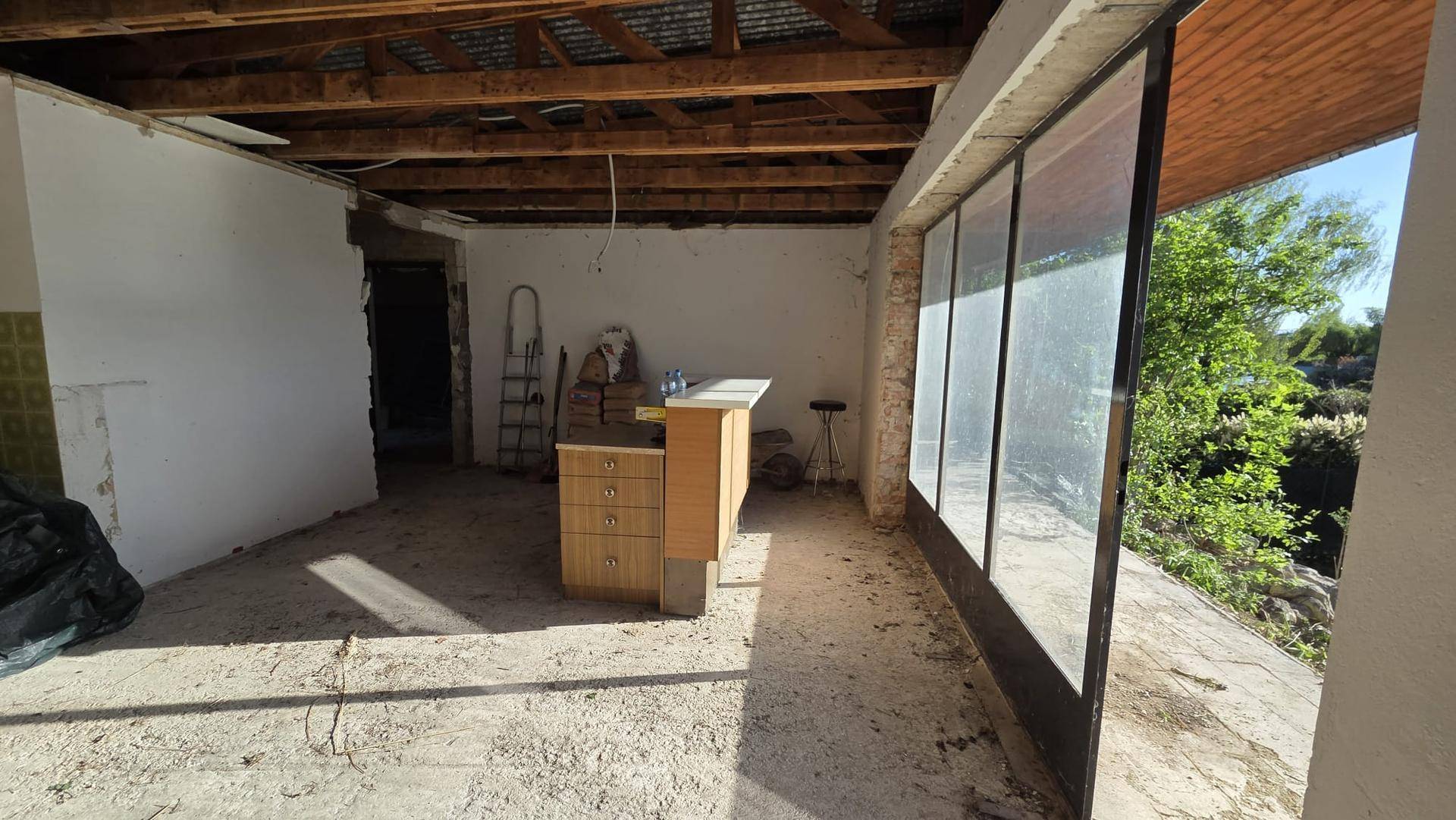 Geräumiger Innenraum im Rohzustand mit Holzbalkendecke und weitem Blick durch die Fenster.