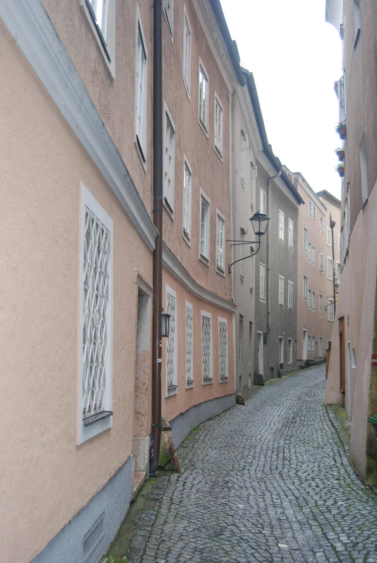 Enge, gepflasterte Gasse zwischen historischen Gebäuden mit unterschiedlichen Fassadenfarben und Fenstern.