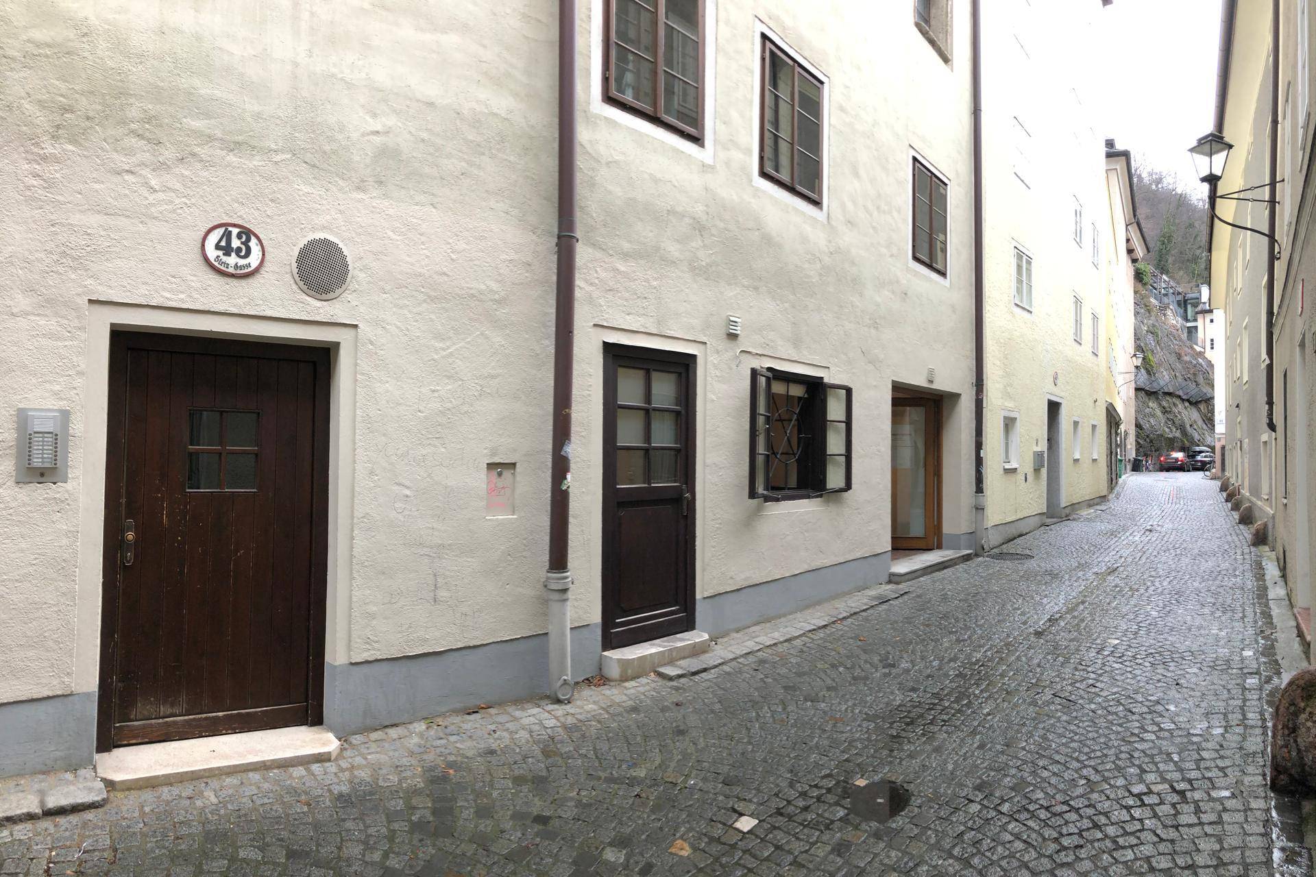Historische Gasse mit Kopfsteinpflaster und mehreren Gebäudeeingängen, darunter eine dunkle Holztür.