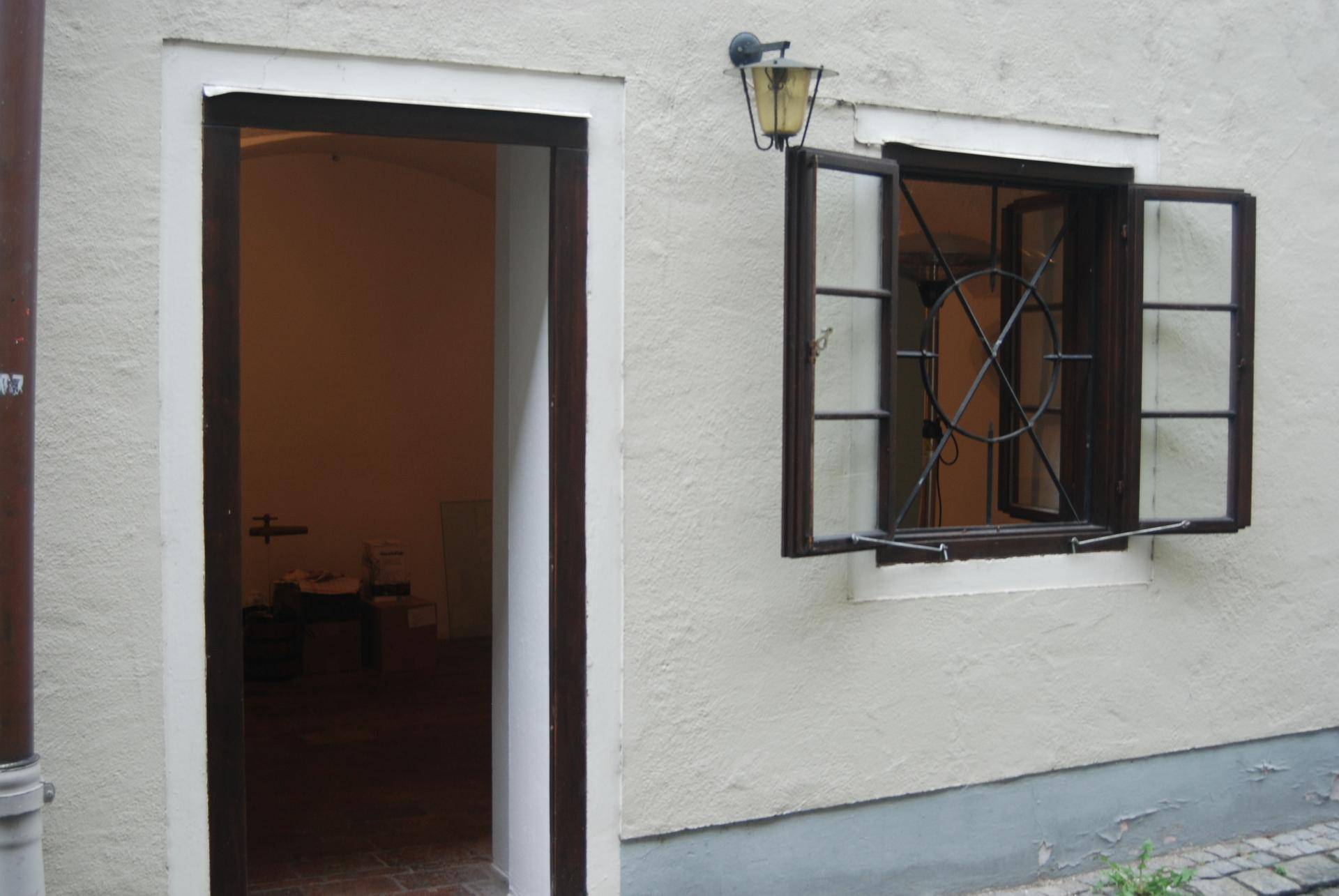 Detailansicht eines Hauseingangs mit offener Tür und einem Fenster mit dekorativem Gitter.