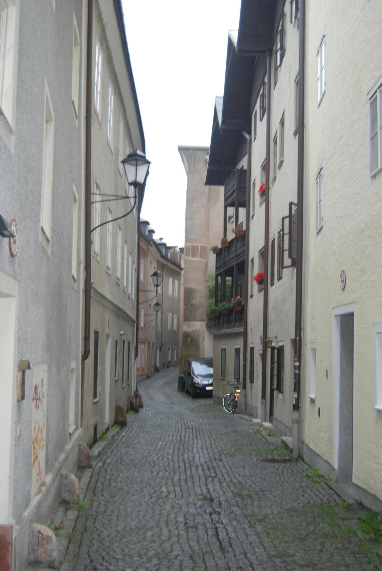Historische Gasse mit Kopfsteinpflaster, gesäumt von alten Gebäuden und einem geparkten Auto.