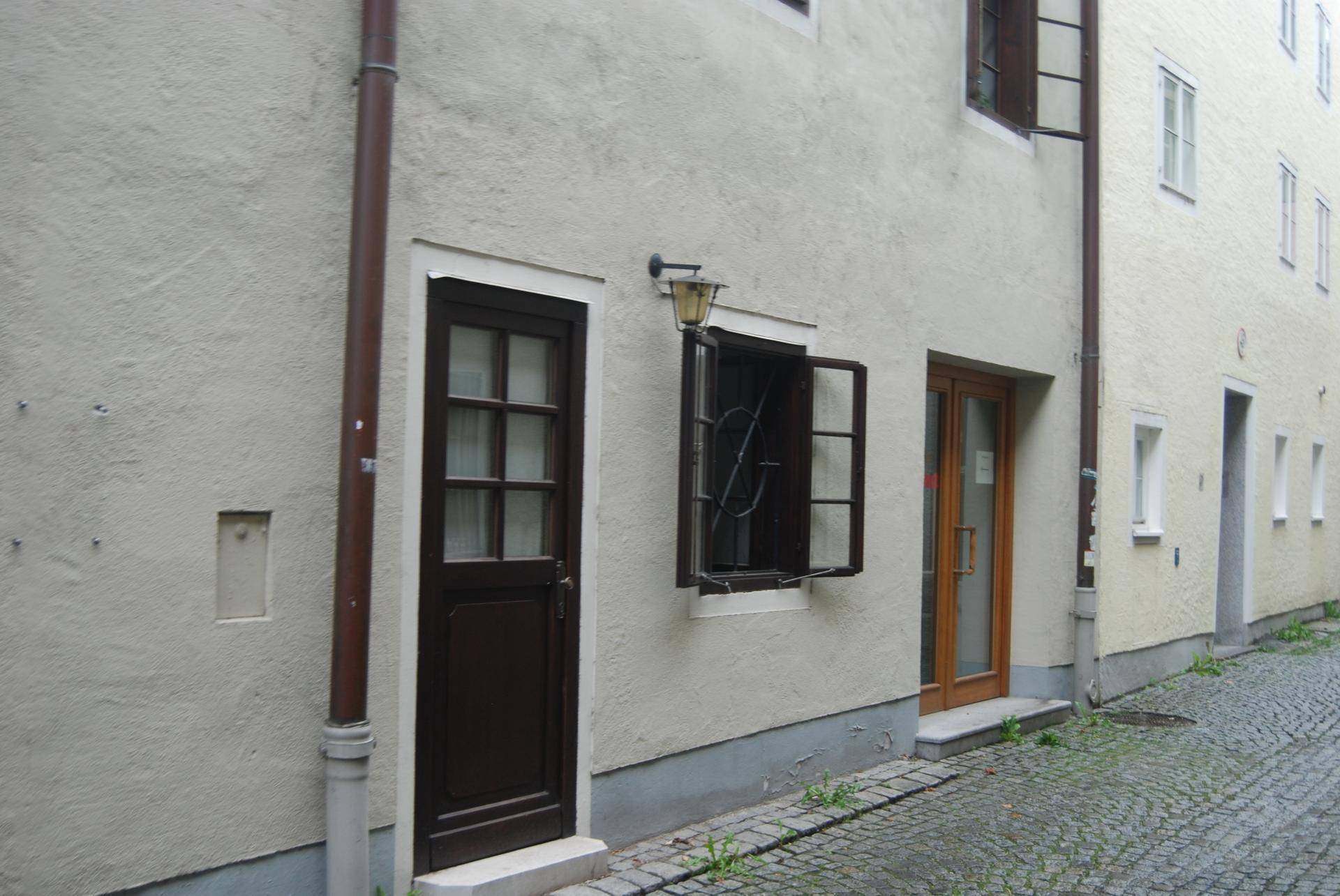 Historische Gasse mit Kopfsteinpflaster und mehreren Gebäudefassaden, darunter ein dunkler Holzeingang.