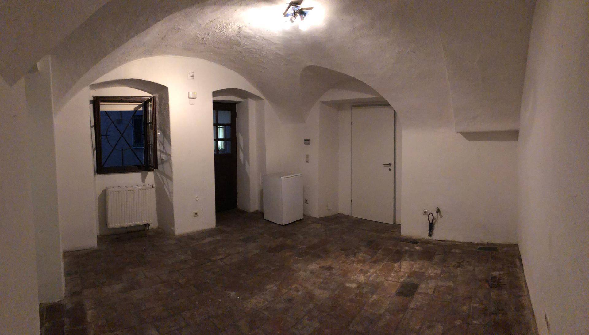 Kellerraum mit gewölbter Decke, Ziegelboden, einem Fenster mit Gitter und einem Heizkörper.