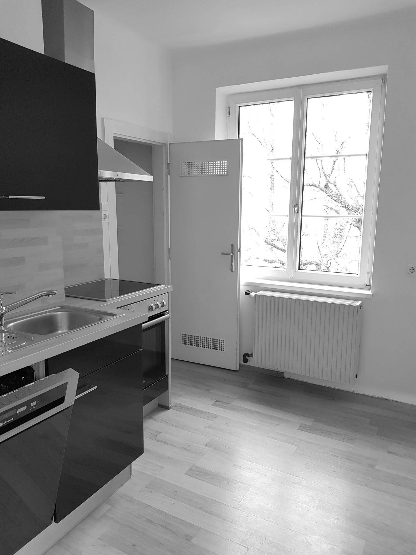 Moderne Küche mit dunklen Schränken, Spüle, Kochfeld und Fenster, in Schwarz-Weiß dargestellt.