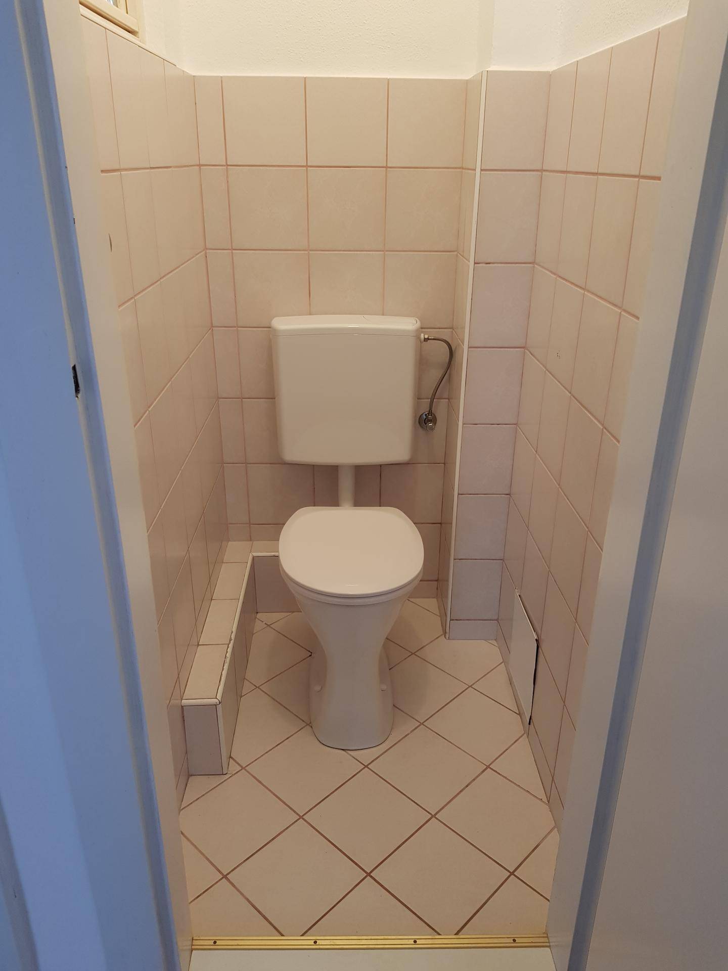 Kleines separates WC mit weißer Toilette und hellen Fliesen an Wänden und Boden.